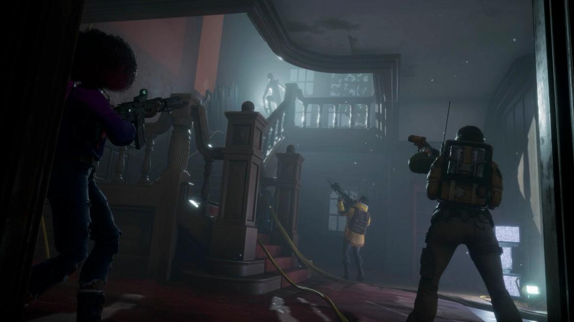 Screenshot of Redfall players standing at the bottom of a dark staircase holding their guns